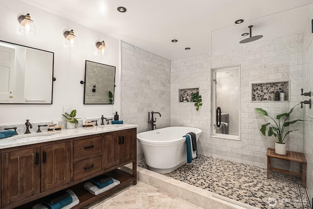 full bath featuring double vanity, tile walls, a walk in shower, a freestanding bath, and a sink