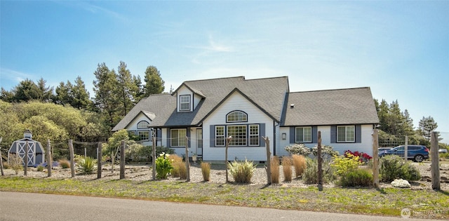 view of front of home featuring an outdoor structure, a shingled roof, and a storage shed
