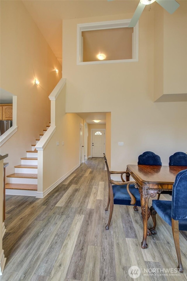 dining area featuring ceiling fan, wood finished floors, stairway, baseboards, and a high ceiling