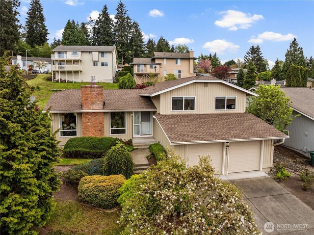 split level home featuring a shingled roof, an attached garage, a chimney, and driveway