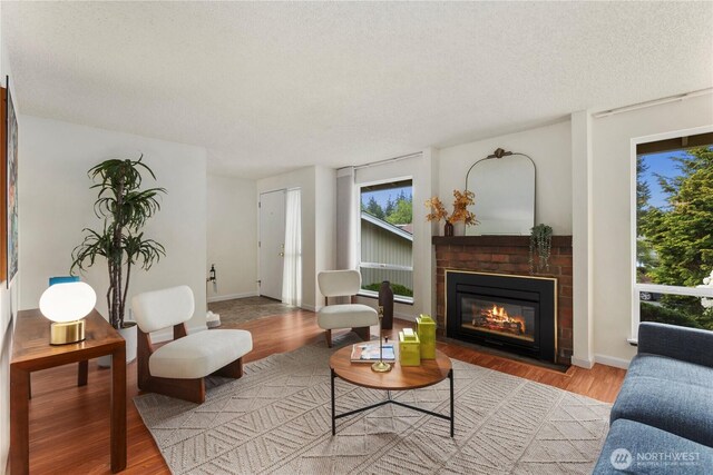 living area featuring a brick fireplace, a textured ceiling, baseboards, and wood finished floors