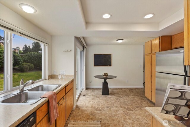 kitchen with stone finish floor, brown cabinets, a sink, a raised ceiling, and freestanding refrigerator