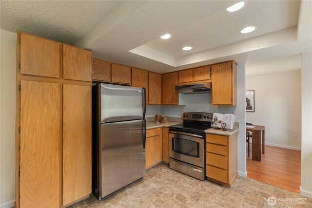 kitchen with appliances with stainless steel finishes, a raised ceiling, light countertops, recessed lighting, and under cabinet range hood