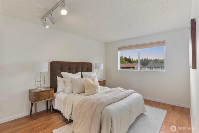 bedroom with a textured ceiling, baseboards, rail lighting, and wood finished floors