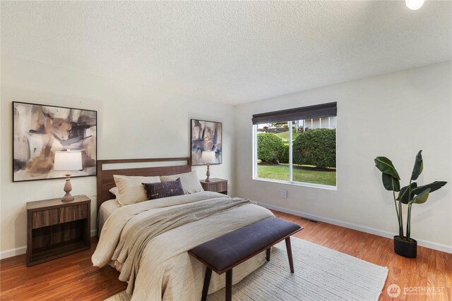 bedroom with baseboards, a textured ceiling, wood finished floors, and visible vents