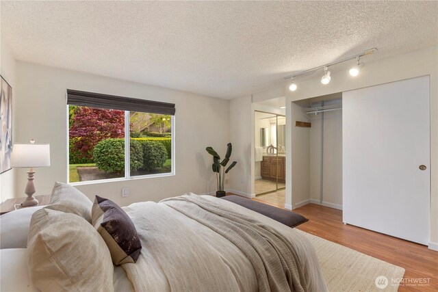 bedroom featuring a textured ceiling, track lighting, light wood-style flooring, and ensuite bath