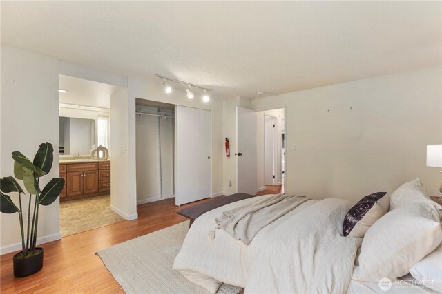 bedroom with a sink, baseboards, track lighting, a closet, and light wood-style floors
