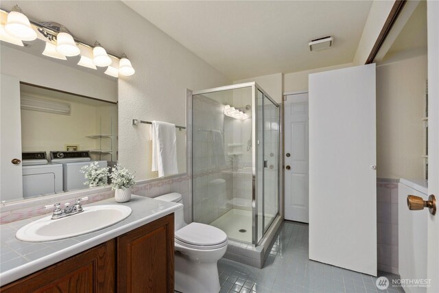 bathroom featuring washer and dryer, toilet, tile patterned flooring, and a stall shower