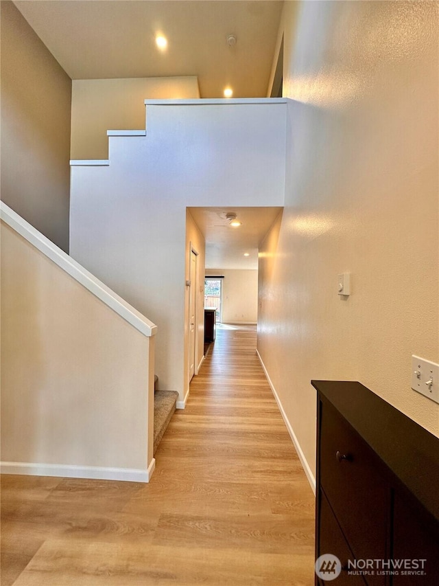 corridor with recessed lighting, baseboards, light wood finished floors, and stairs