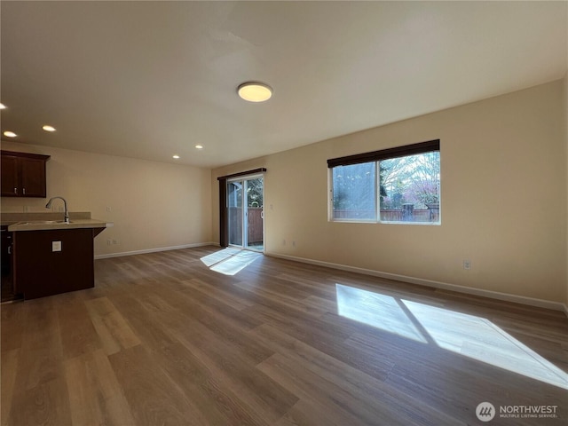 unfurnished living room with recessed lighting, baseboards, a sink, and wood finished floors