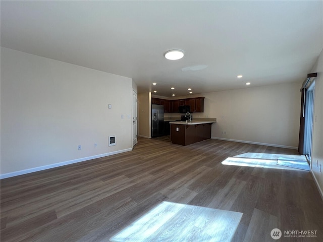 unfurnished living room with recessed lighting, baseboards, a sink, and wood finished floors