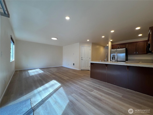 kitchen with stainless steel refrigerator with ice dispenser, light countertops, baseboards, and light wood finished floors
