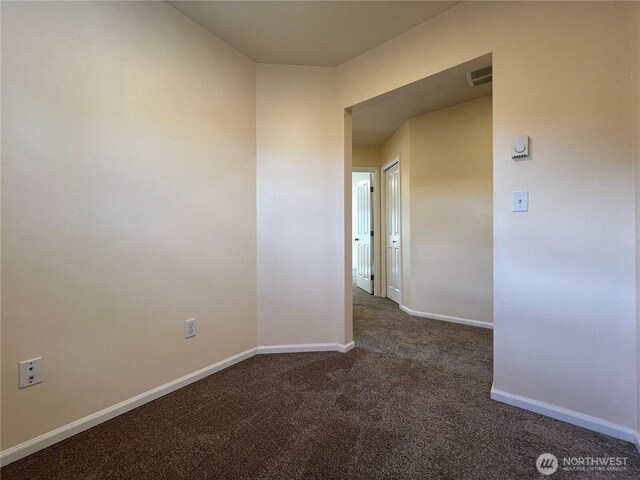 empty room with baseboards, dark colored carpet, and visible vents