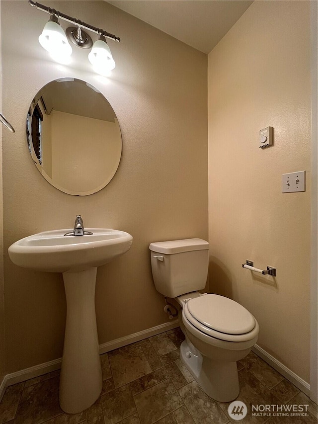 half bath featuring baseboards, a sink, and toilet