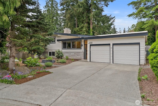 tri-level home with driveway, a chimney, a garage, fence, and stone siding