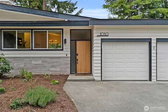 view of exterior entry featuring an attached garage, stone siding, and aphalt driveway