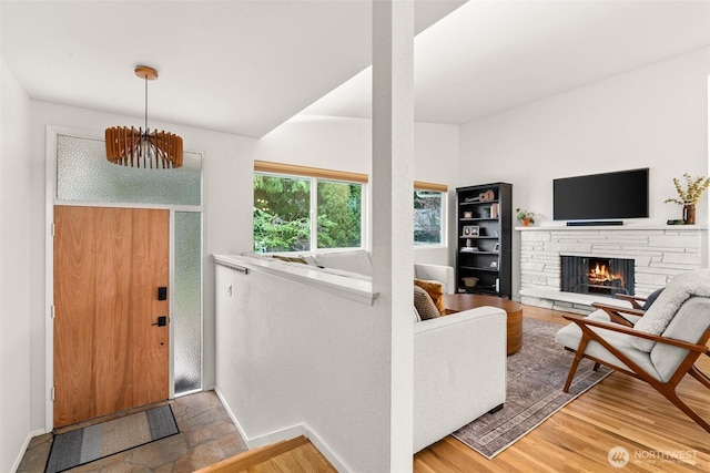 foyer featuring baseboards, a notable chandelier, wood finished floors, and a fireplace