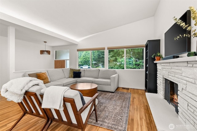 living area with visible vents, light wood-style flooring, lofted ceiling, and a fireplace