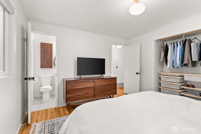 bedroom with light wood-type flooring, connected bathroom, baseboards, and a closet
