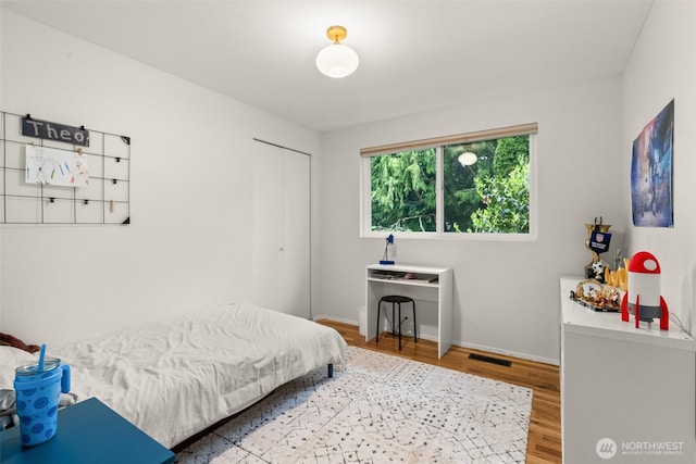 bedroom with baseboards, a closet, wood finished floors, and visible vents