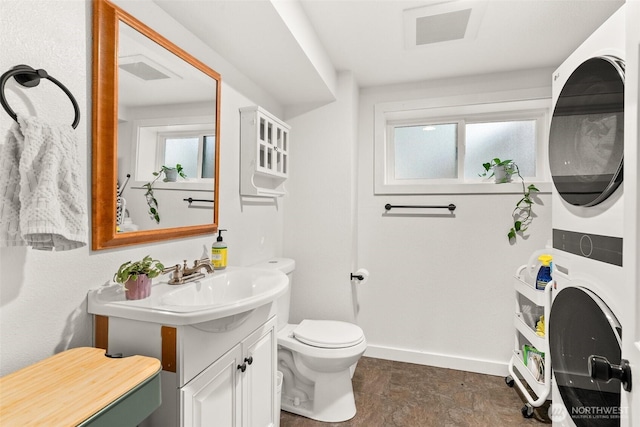 bathroom with vanity, toilet, baseboards, stacked washer / dryer, and visible vents