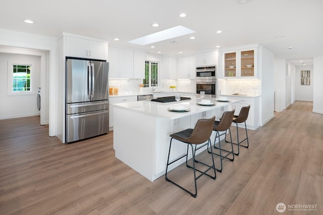 kitchen with a breakfast bar area, white cabinetry, a sink, backsplash, and stainless steel appliances