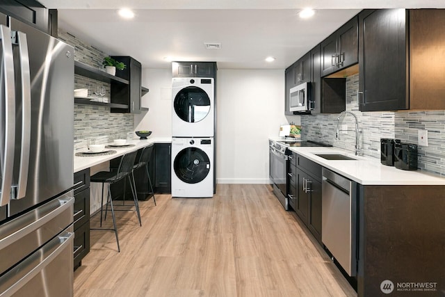 kitchen with decorative backsplash, a sink, light wood finished floors, stacked washer and clothes dryer, and stainless steel appliances