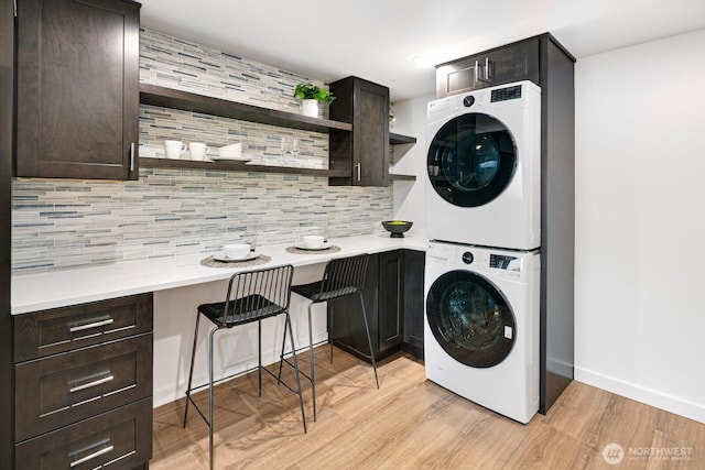 clothes washing area with baseboards, light wood finished floors, and stacked washer and clothes dryer
