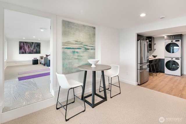 dining room with stacked washer and dryer, light colored carpet, recessed lighting, baseboards, and light wood-type flooring
