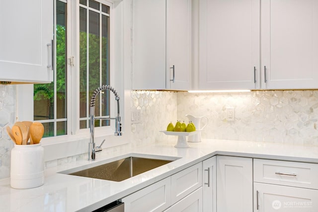 kitchen with a sink, backsplash, white cabinets, and light countertops