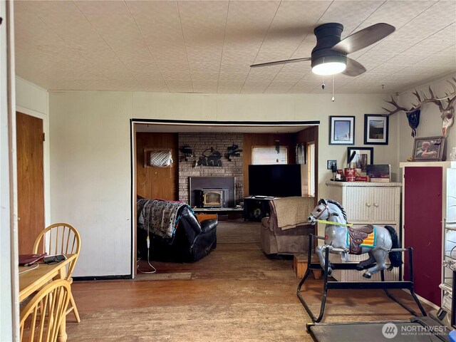 living area featuring ceiling fan, a fireplace, and wood finished floors