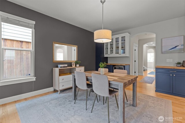 dining space featuring light wood-style floors, arched walkways, and baseboards