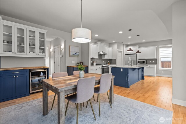 dining space with wine cooler, light wood-style floors, baseboards, recessed lighting, and arched walkways