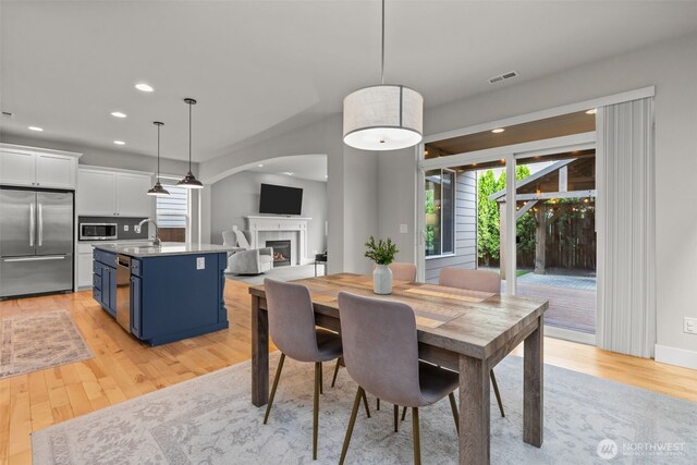dining space featuring visible vents, baseboards, a warm lit fireplace, recessed lighting, and light wood finished floors