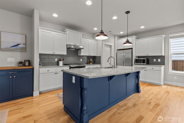 kitchen featuring appliances with stainless steel finishes, a sink, light wood-style floors, tasteful backsplash, and under cabinet range hood