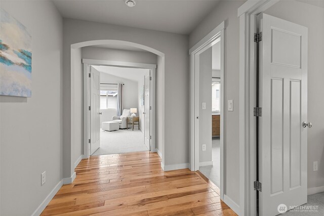 corridor with light wood-style floors, arched walkways, and baseboards