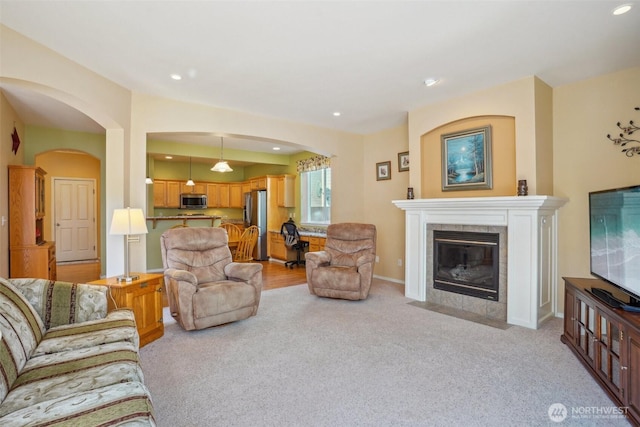 living room with light colored carpet, arched walkways, recessed lighting, and a tile fireplace