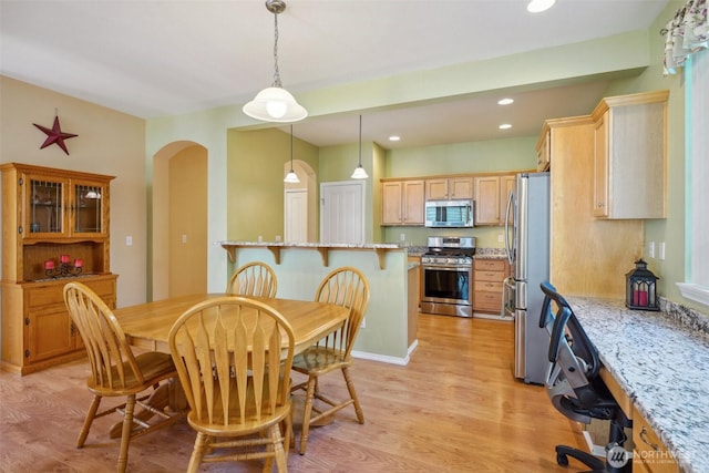 dining room with light wood-style floors, arched walkways, and recessed lighting