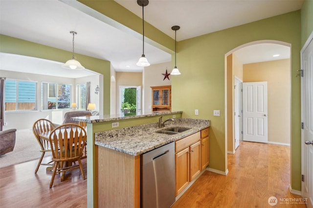 kitchen with arched walkways, stainless steel dishwasher, a sink, light stone counters, and light wood finished floors