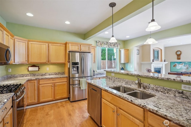 kitchen featuring pendant lighting, appliances with stainless steel finishes, a sink, light stone counters, and light wood-style flooring
