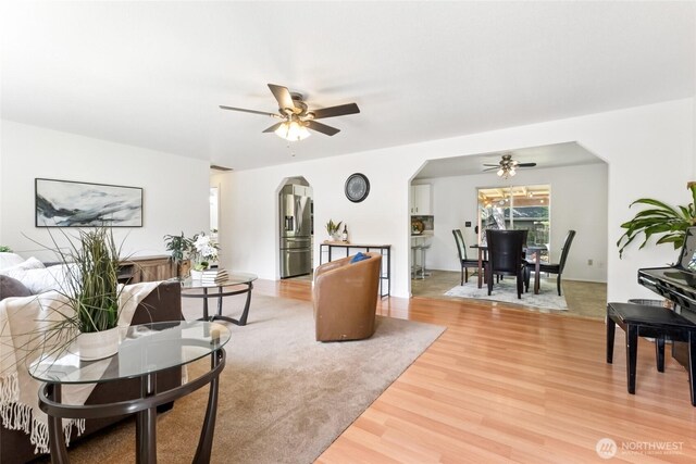 living room featuring a ceiling fan, arched walkways, and light wood finished floors