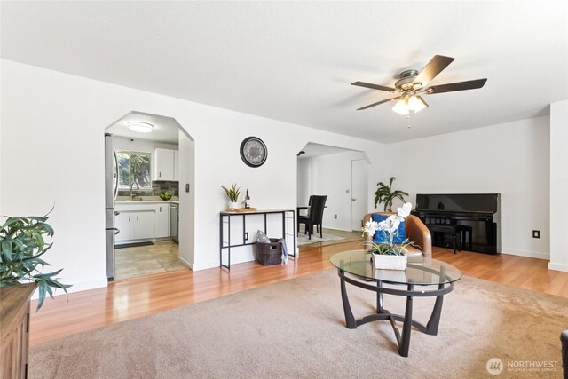 living room with a ceiling fan, arched walkways, and light wood-style flooring