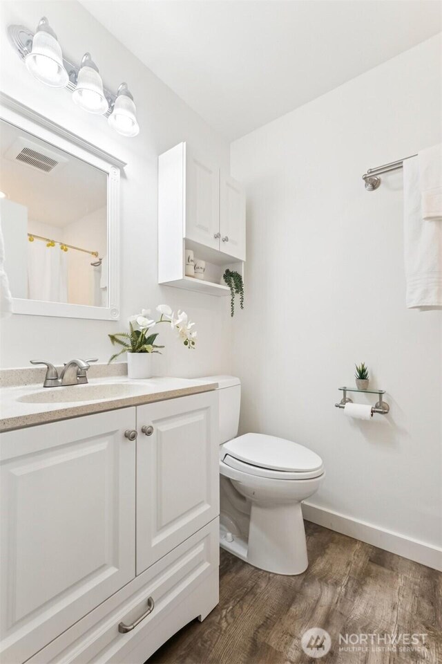bathroom featuring a shower with curtain, visible vents, wood finished floors, vanity, and toilet