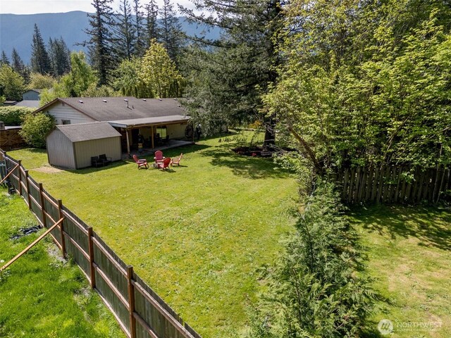 view of yard featuring a storage shed, a forest view, an outbuilding, and a fenced backyard