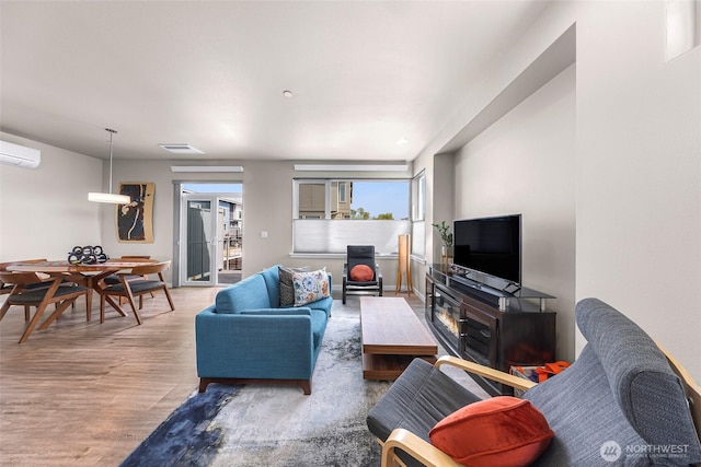 living area featuring visible vents, a wood stove, wood finished floors, and a wall mounted air conditioner