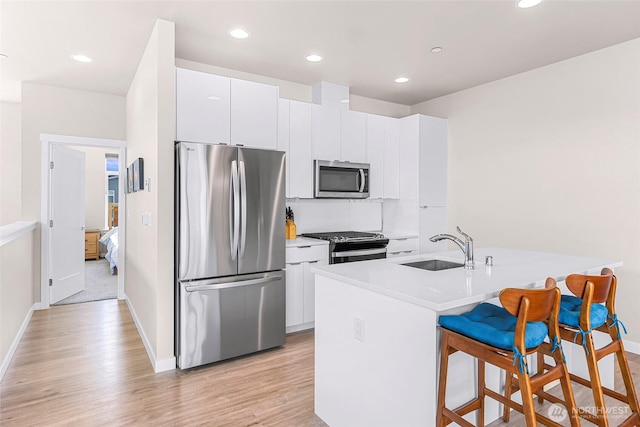 kitchen with a sink, light countertops, light wood-style floors, a breakfast bar, and stainless steel appliances