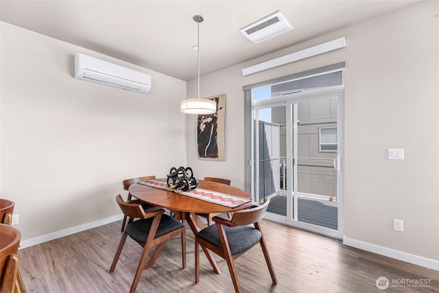 dining space with an AC wall unit, baseboards, wood finished floors, and visible vents