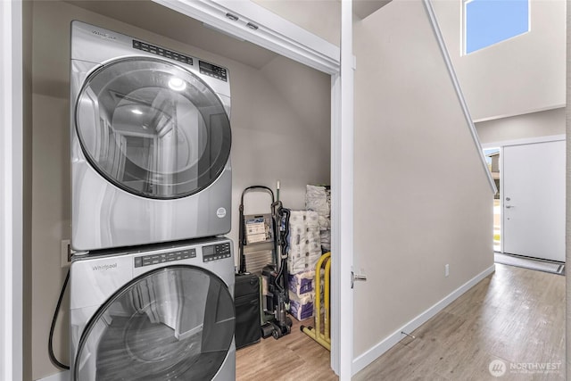 clothes washing area featuring baseboards, stacked washer / drying machine, wood finished floors, and laundry area