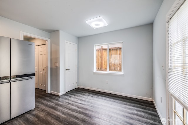 unfurnished bedroom featuring baseboards, multiple windows, freestanding refrigerator, and dark wood-type flooring