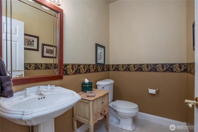 bathroom with tile patterned flooring, wainscoting, a sink, baseboards, and toilet